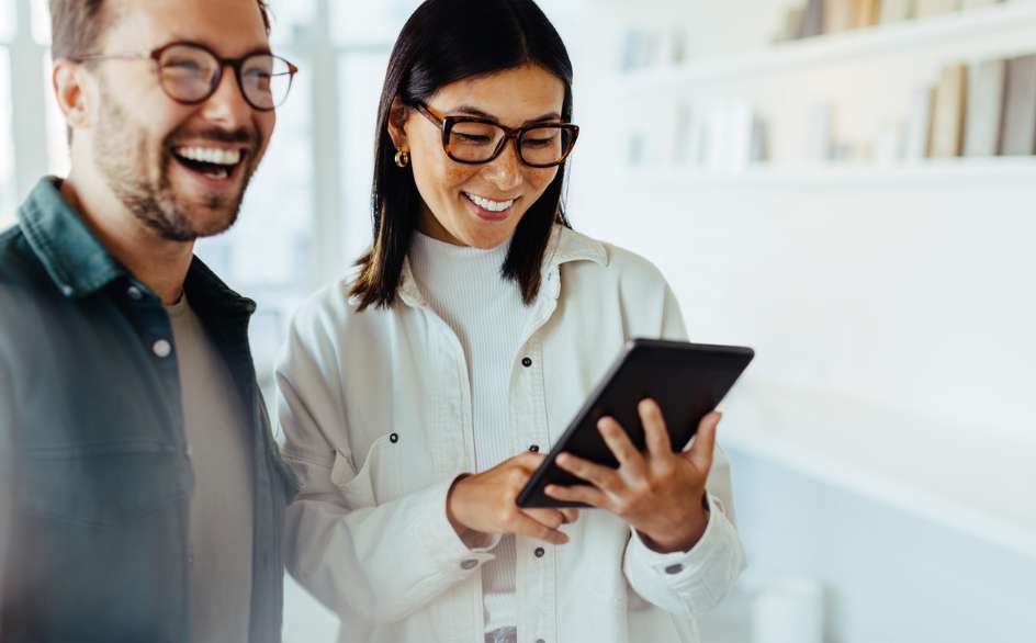 Man and woman looking at a tablet, smiling in informal workwear.